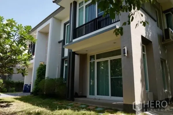 Detached House for sale in Pak Kret, Nonthaburi - Rear facade of the house with balcony, sliding doors and a lawn garden.