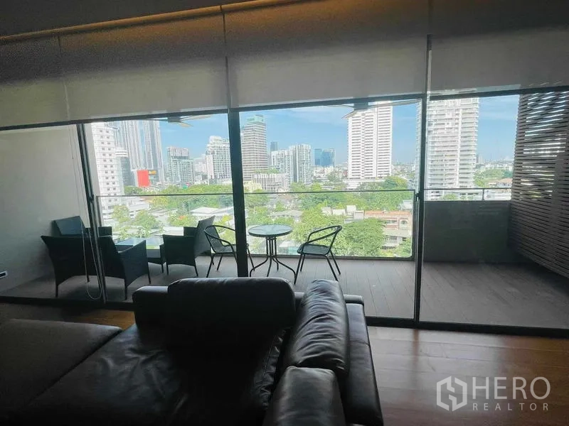 คอนโด ให้เช่าหรือขายในWatthana, Bangkok - ระเบียงปกคลุมพร้อมชุดโต๊ะเก้าอี้ มองเห็นวิวสกายไลน์ผ่านกระจกเต็มบาน