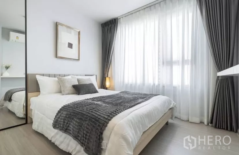 Condominium for rent in Chatuchak, Bangkok - Second bedroom with large window, full‑height mirror and layered bedding.