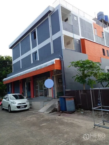 Retail Space for sale in Lam Luk Ka, Pathum Thani - Angled exterior view of grey-and-orange retail block with parking area and trees.