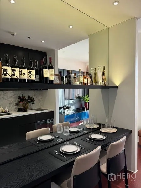 Condominium for sale in Watthana, Bangkok - Dining corner with soft ceiling lights, mirror wall and a floating shelf above, adjoining the modern kitchen.