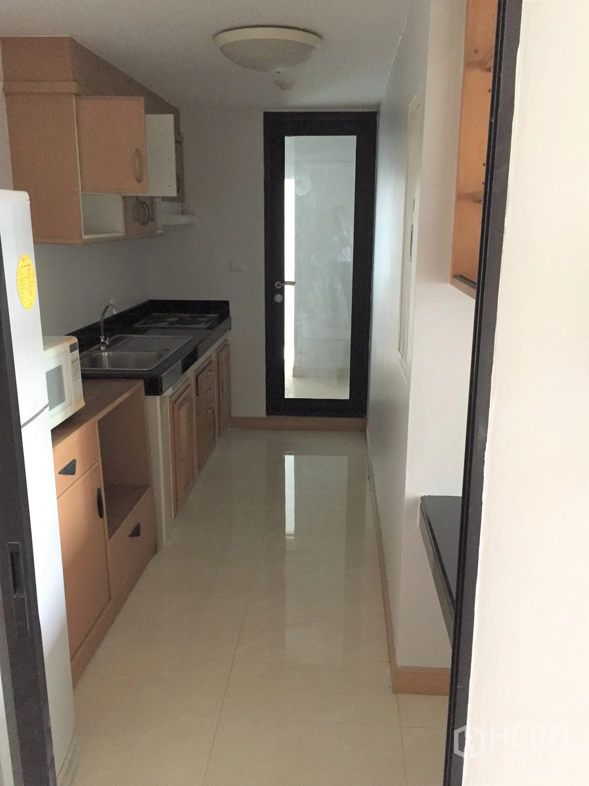 คอนโด ให้เช่าในWatthana, Bangkok - ครัวแยกสไตล์แกลเลย์ พร้อมตู้ไม้ ไมโครเวฟ อ่างล้างจาน ท็อปสีดำ และประตูกระจกสู่ระเบียง