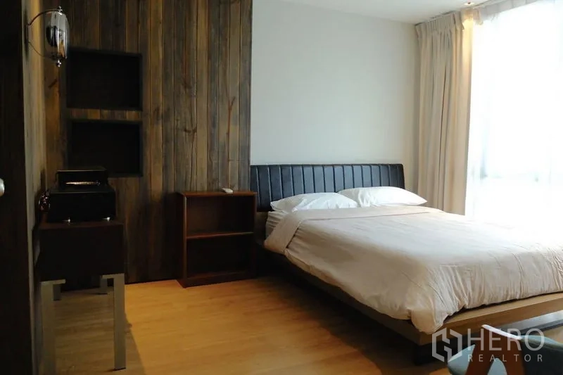 Condominium for sale in Watthana, Bangkok - Bright bedroom with wood panel feature wall and a queen bed near a large window.