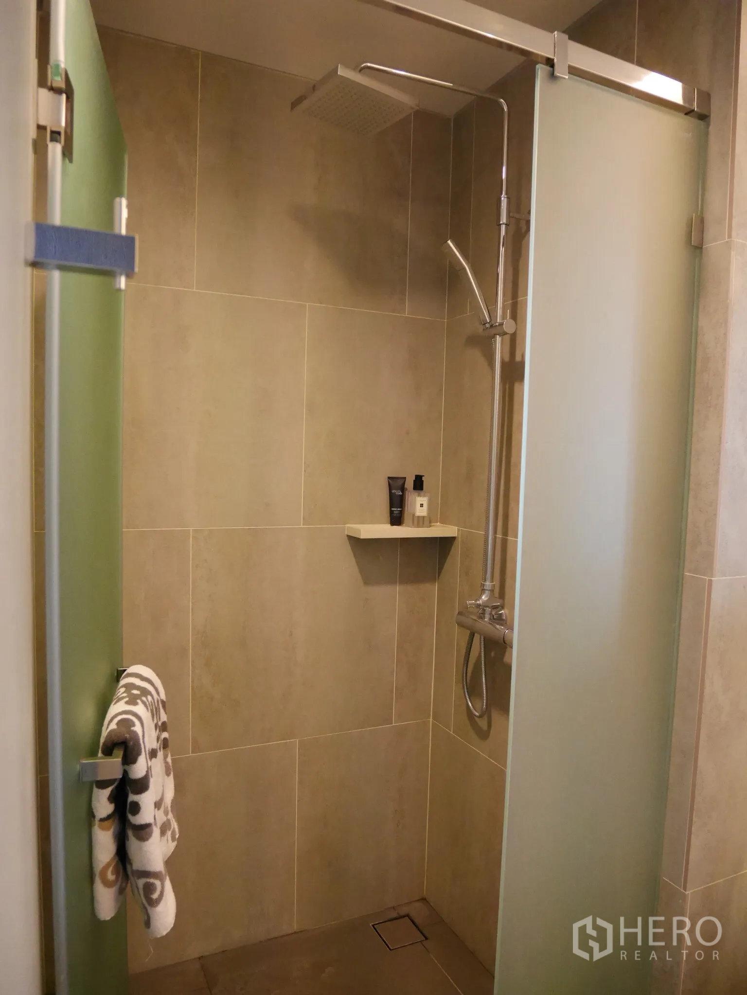 Condominium for rent in Khlong Toei, Bangkok - Modern bathroom with rain shower and frosted glass enclosure, finished in beige tiles.