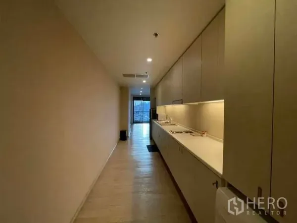 公寓 出租在Watthana, Bangkok - 走廊式厨房通向带阳台的起居区，暖色筒灯照明。