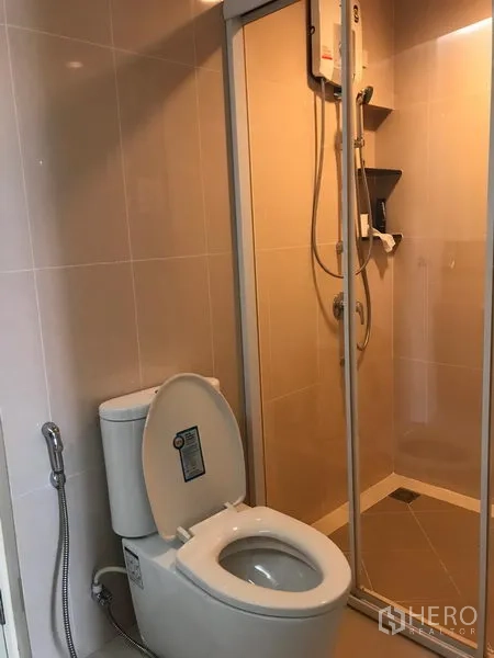 Townhouse for rent or sale in Bang Kho Laem, Bangkok - Bathroom with glass-enclosed shower, toilet with spray hose and tiled walls.