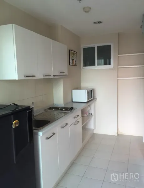 Condominium for rent in Bang Rak, Bangkok - Compact white kitchenette with cabinets, sink, cooktop, microwave and refrigerator.