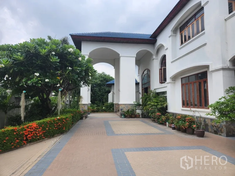 独立式住宅 出租在Prawet, Bangkok - 入口一侧拱形门廊，修剪整齐的花篱与宽阔车道。