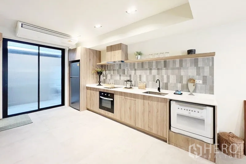 联排别墅 出租在Khlong Toei, Bangkok - 明亮厨房，浅木色橱柜、瓷砖背墙、烤箱、冰箱与推拉玻璃门。