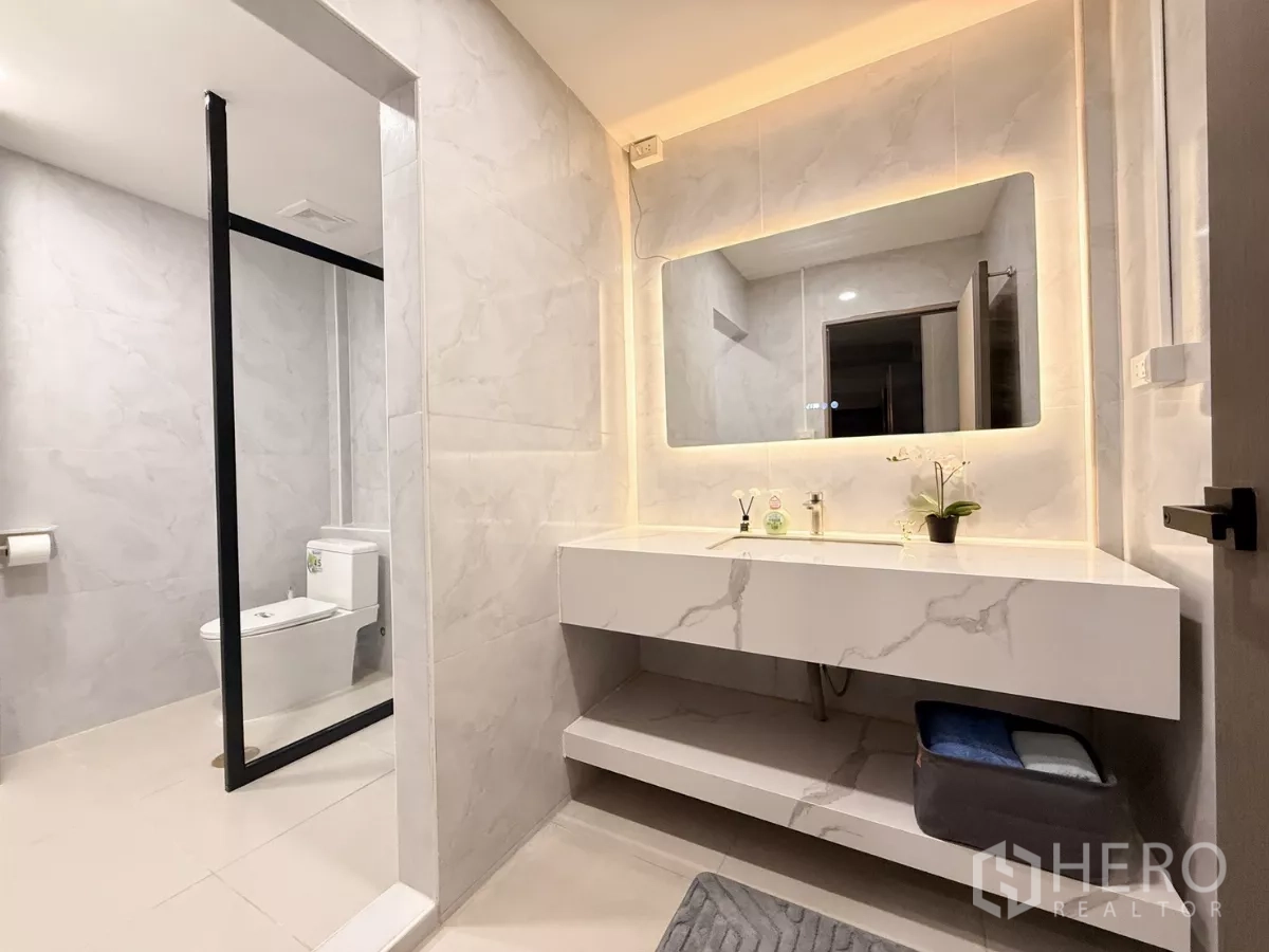 店屋 出租在Ratchathewi, Bangkok - 现代浴室台面与背光镜，旁为玻璃隔断淋浴和马桶。