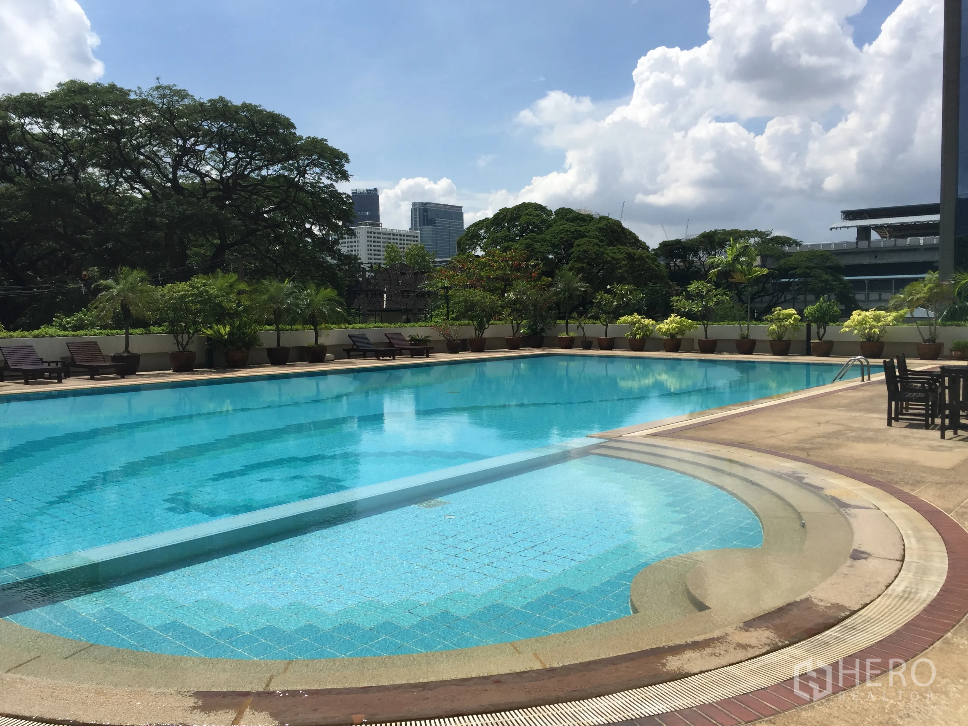 Condominium for rent in Pathum Wan, Bangkok - Large outdoor swimming pool with sunbeds and greenery against the Bangkok skyline.