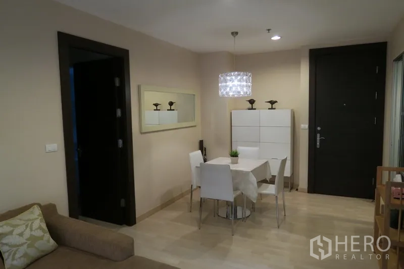 Condominium for rent in Huai Khwang, Bangkok - Cozy dining corner with four‑seat table under a crystal pendant light near the entry door and wall mirror.