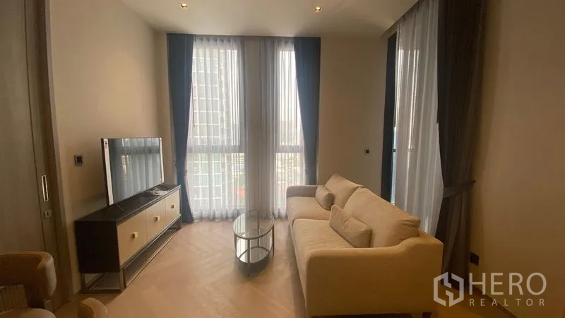 Condominium for rent - Wide shot of living room featuring sofa, TV stand and two tall draped windows.