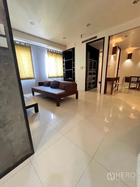 Condominium for rent in Ratchathewi, Bangkok - Sunlit living area with tiled floors, sofa, and view toward the dining zone through open partitions.