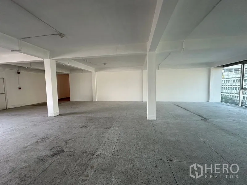 Office Space for rent in Khlong Toei, Bangkok - Open workspace with structural columns, large corner glazing and gray tiled floor.