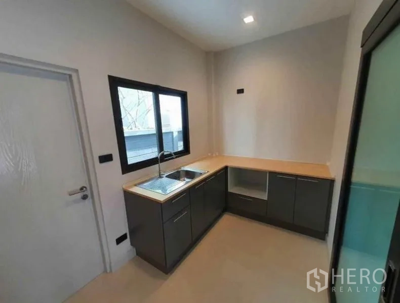 Detached House for rent in Lak Si, Bangkok - Compact L-shaped kitchen with window, sink, dark cabinetry and light countertops.