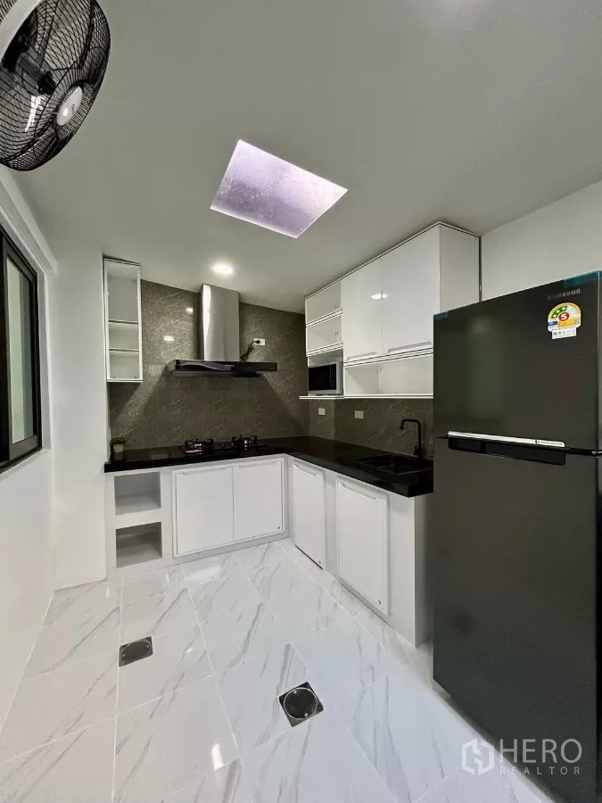 Townhouse for rent in Bang Phli, Samut Prakan - L-shaped kitchen with white cabinets, black countertop, hob, hood and fridge.