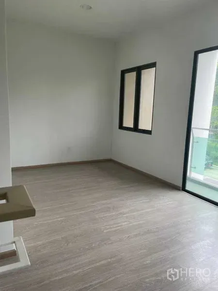 Townhouse for sale in Bueng Kum, Bangkok - Empty room with wood-look flooring beside a balcony with glass railing.