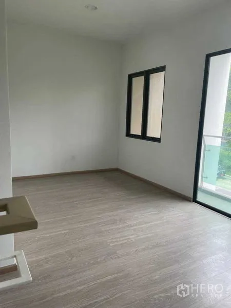 Townhouse for sale in Bueng Kum, Bangkok - Empty room with wood-look flooring beside a balcony with glass railing.