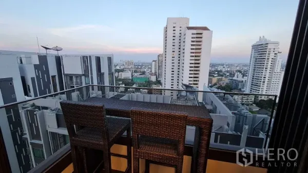 Condominium for rent in Watthana, Bangkok - High-floor balcony with bar stools and a panoramic Bangkok skyline at dusk.