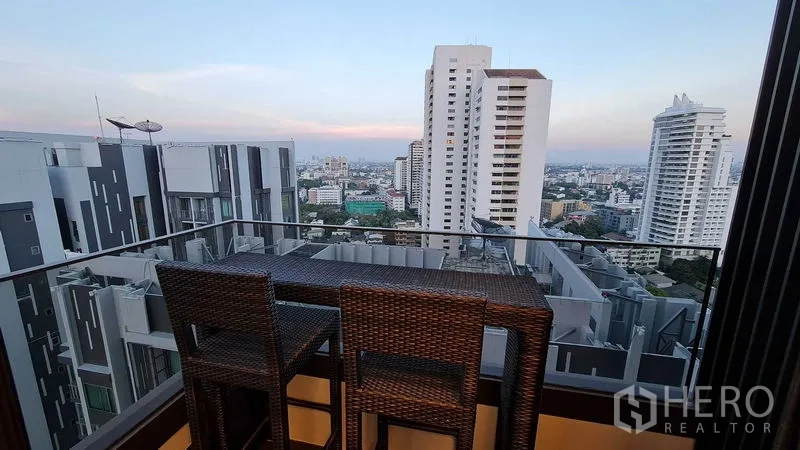 Condominium for rent in Watthana, Bangkok - High-floor balcony with bar stools and a panoramic Bangkok skyline at dusk.