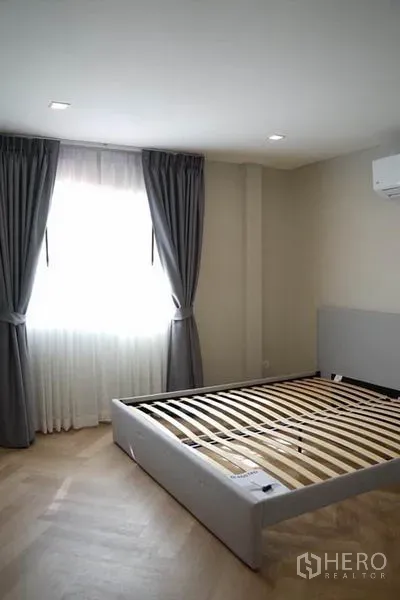 Detached House for rent in Wang Thonglang, Bangkok - Air-conditioned bedroom with large window, grey curtains and a bed frame.