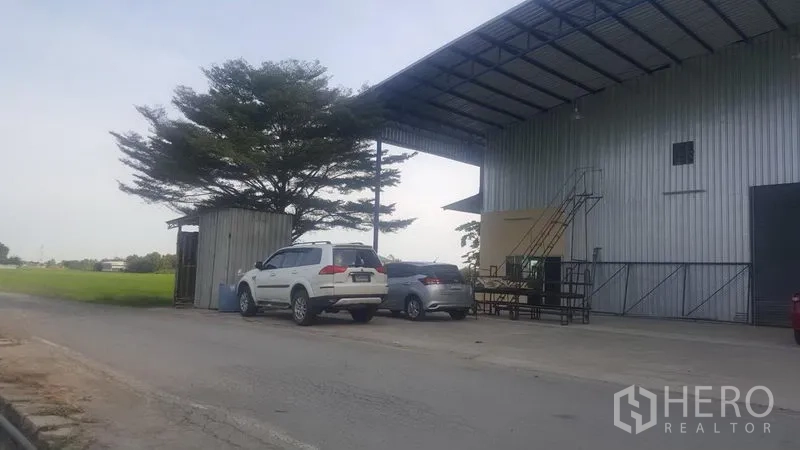工厂 出租在Khlong Luang, Pathum Thani - 临路入口视角，带遮雨装卸区、路边停车位与绿地