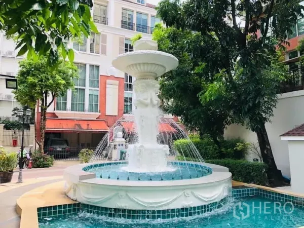 Townhouse for rent in Khlong Toei, Bangkok - Elegant courtyard fountain surrounded by landscaping in front of low-rise townhouse buildings.