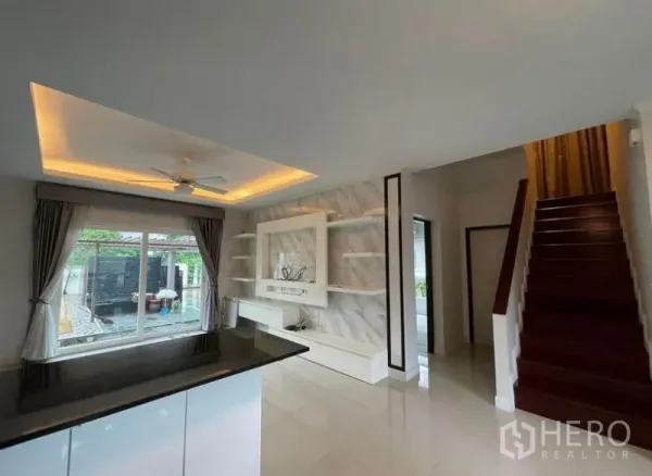 独立式住宅 出售在Bang Phli, Samut Prakan - 从吧台望向电视特色墙、楼梯和可见泳池的窗户。