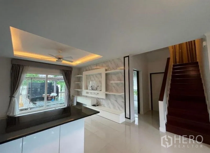 独立式住宅 出售在Bang Phli, Samut Prakan - 从吧台望向电视特色墙、楼梯和可见泳池的窗户。