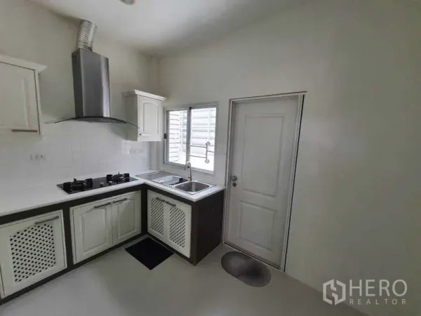 Detached House for rent in Saphan Sung, Bangkok - Compact white kitchen with gas hob, chimney hood, sink and side door by a window.
