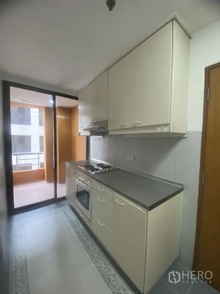 คอนโด ให้เช่าในPathum Wan, Bangkok - ครัวแบบแกลลอรี่ ตู้บิลท์อินสีขาว เตาและเตาอบ พร้อมประตูกระจกออกสู่ระเบียงซักล้าง