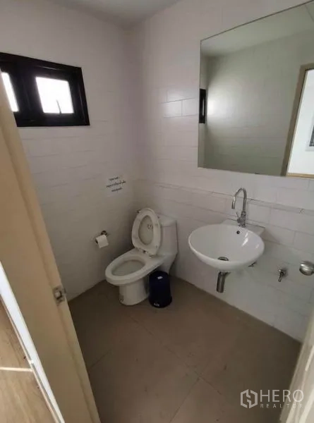 Home Office for rent in Prawet, Bangkok - White tiled bathroom with toilet, wall mirror, sink, and small window