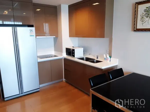 Condominium for rent in Khlong Toei, Bangkok - Modern Phra Khanong condo kitchen with glossy cabinets, double-door fridge, and built-in cooktop.