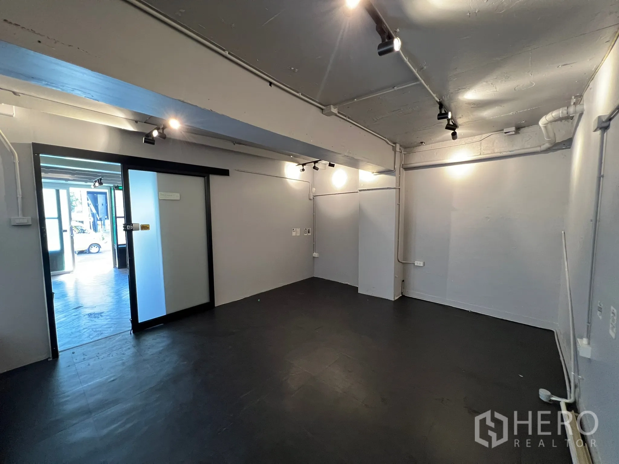 零售空间 出租在Watthana, Bangkok - 室内空旷空间，外露管线与轨道灯，灰色墙面，带推拉玻璃门