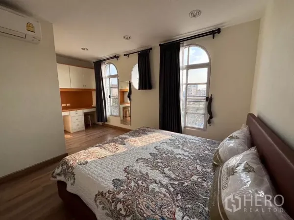 Townhouse for rent in Bang Kho Laem, Bangkok - Master bedroom with arched windows, built-in desk and storage on a wooden floor.