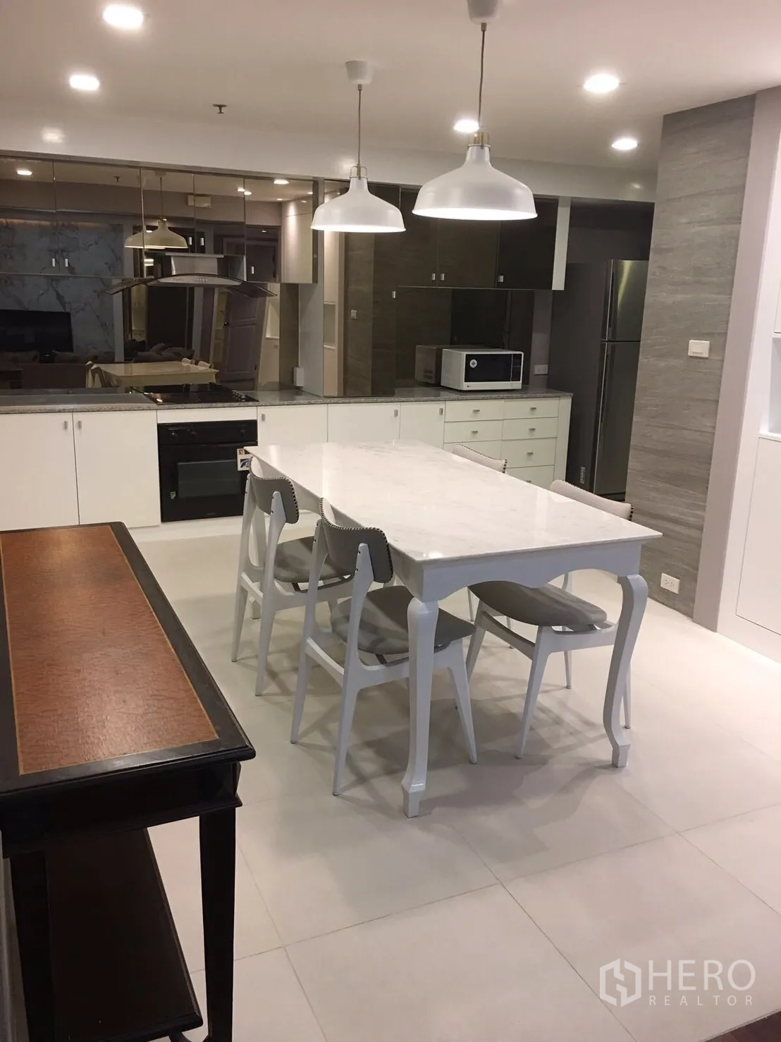 Condominium for rent in Watthana, Bangkok - Open-plan kitchen with white cabinetry, marble dining table, pendant lights, built-in oven and stainless fridge in a Sukhumvit condo.