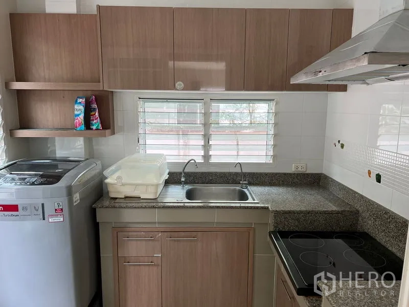 Detached House for rent in Bang Kapi, Bangkok - Fitted kitchen with granite countertops, electric cooktop, range hood, sink, and washing machine.