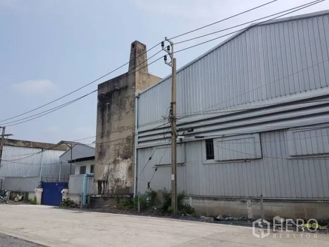 Factory for rent or sale in Bang Phli, Samut Prakan - Factory facade with ribbed metal cladding and power poles beside a weathered concrete tower.