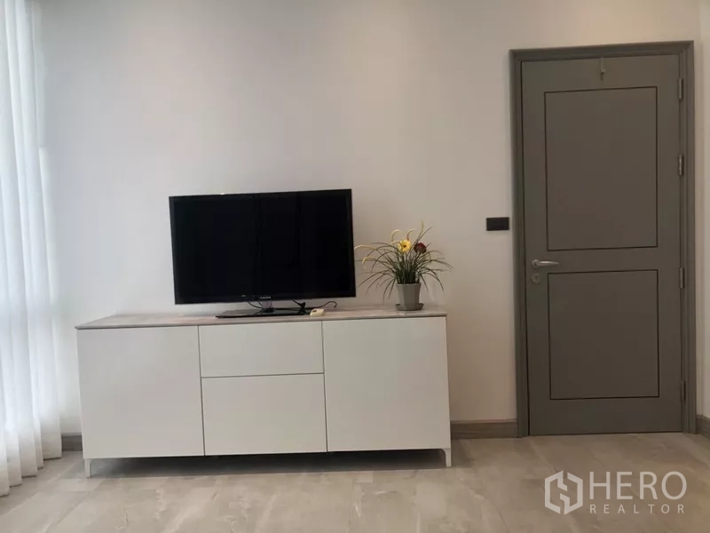 公寓 出租在Sathon, Bangkok - 极简电视柜摆放小电视与绿植，旁为灰色门，采光充足。