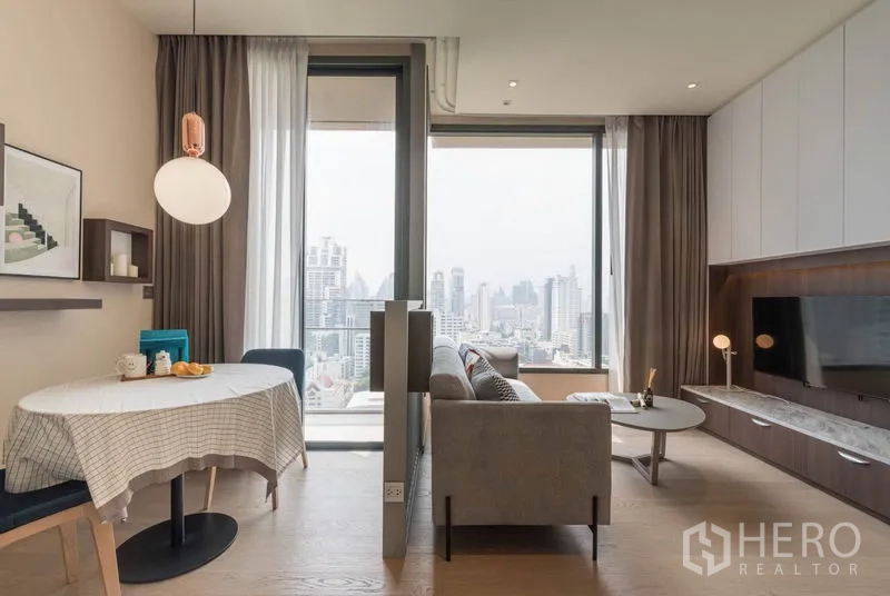 Condominium for rent in Watthana, Bangkok - Dining corner and lounge with full-height windows and skyline panorama, plus a TV wall with storage.