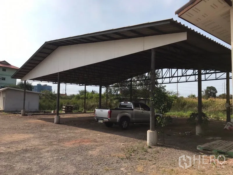 Land for sale in Mueang Samut Sakhon, Samut Sakhon - Close‑up of open‑sided steel‑roof shed with a pickup truck and an outbuilding in the background.