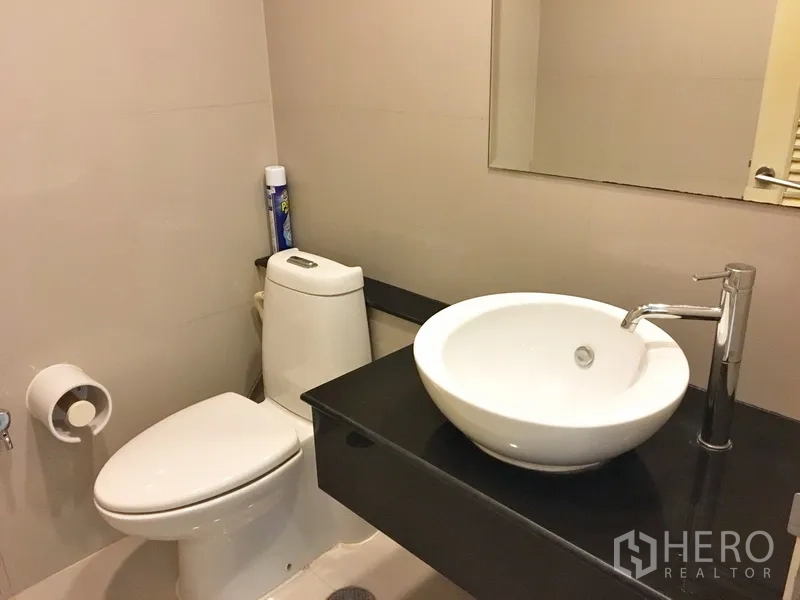 Condominium for rent in Khlong Toei, Bangkok - Guest bathroom with round vessel sink, mirror, and toilet in neutral tones.