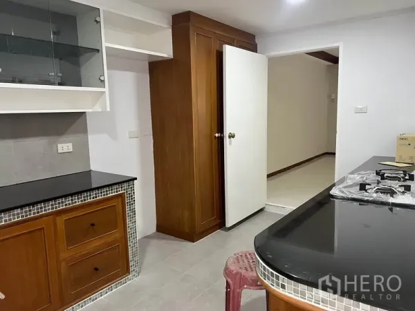 Townhouse for rent in Watthana, Bangkok - Closed kitchen with wooden cabinetry, black stone countertops, and a gas hob.