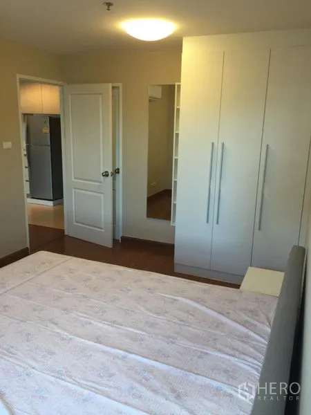 Condominium for rent in Huai Khwang, Bangkok - Bright bedroom with built-in wardrobe, full-length mirror and wood floors.