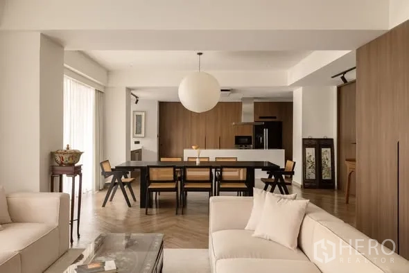 Condominium for sale in Khlong Toei, Bangkok - Wide shot of open living and dining space with sofas, long table and modern kitchen backdrop.