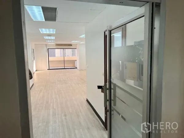 办公空间 出租在Pathum Wan, Bangkok - 从玻璃入口望向长形办公区，吊顶灯带，尽头为阳台。