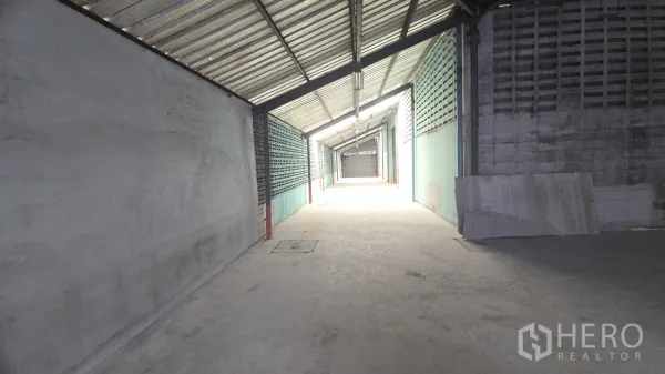 Warehouse for rent in Khlong Sam Wa, Bangkok - Long side aisle with metal roof and ventilated block walls ending at a roller door.