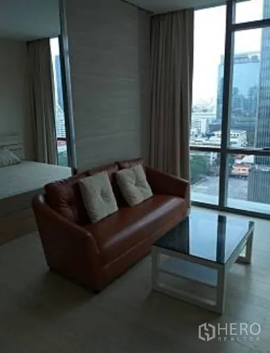 公寓 出租在Watthana, Bangkok - 客厅配皮沙发与玻璃茶几，落地窗俯瞰城市天际线。