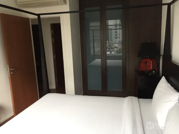 Condominium for rent or sale in Watthana, Bangkok - Bright bedroom with white bedding, built-in wardrobe, bedside lamp and air conditioner.